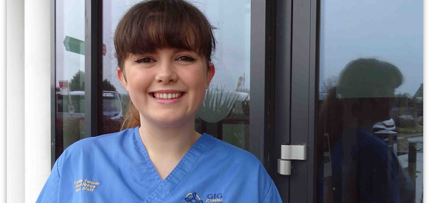 Close up head and shoulders picture of nurse wearing scrubs standing in front of glass door