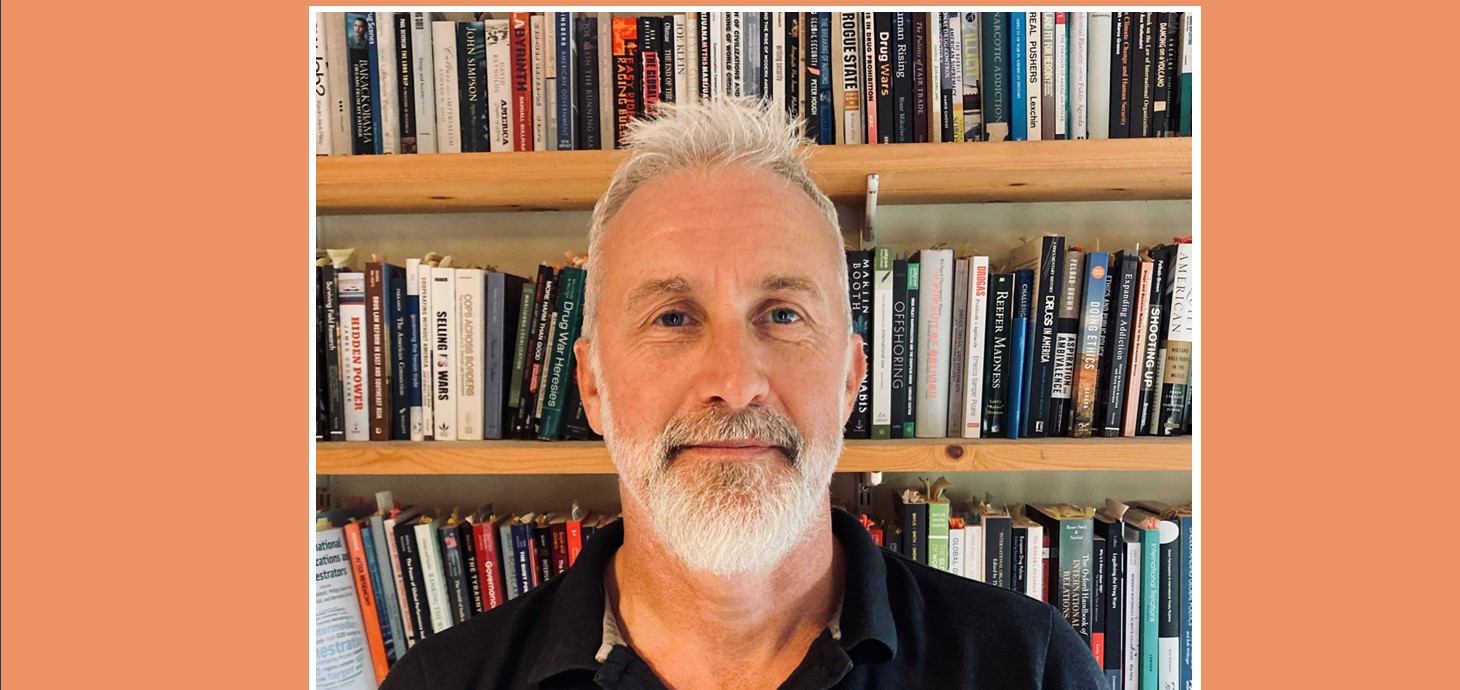 Head and shoulders photo of bearded man in front of bookcase.