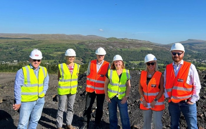 Six people wearing high-viz jackets and hard hats outside on a hilltop site