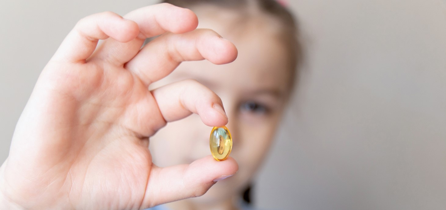 A child holding up an omega-3 supplement.