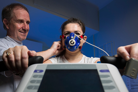 Woman wearing oxygen mask sitting on exercise bike with man by her side