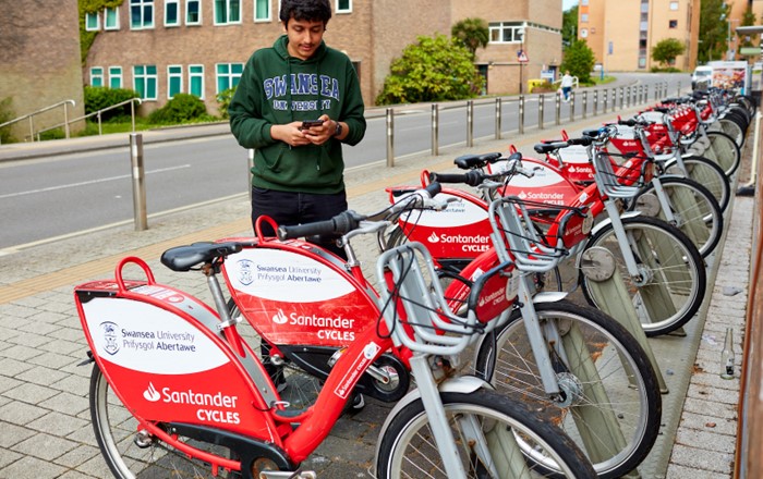 A student standing outside by a row of red bicycles