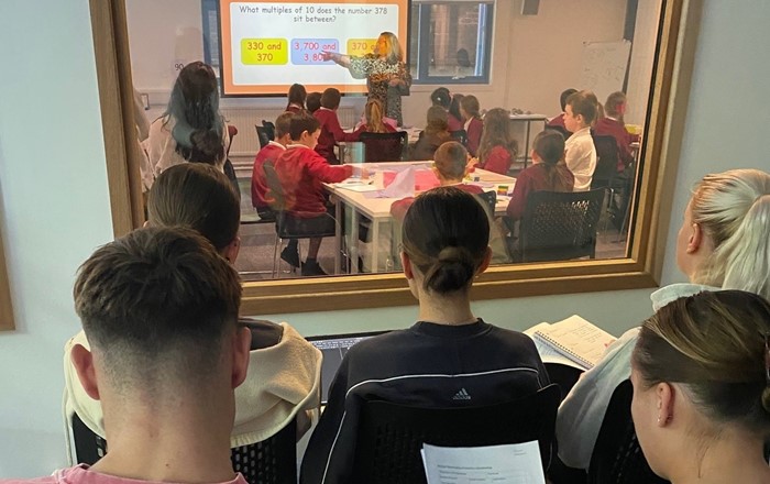 A group of student teachers using an observational classroom to watch a teacher's questioning in mathematics.