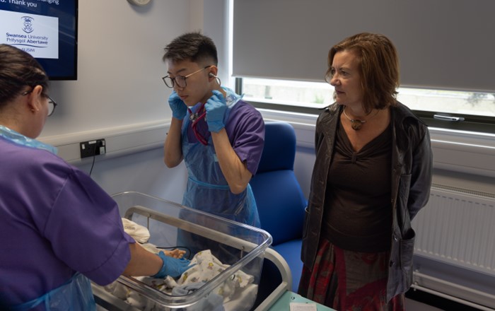 First Minister of Wales, Eluned Morgan MS, is watching two nursing students practicing baby care in the Simulation and Immersive Learning Centre at Swansea University.