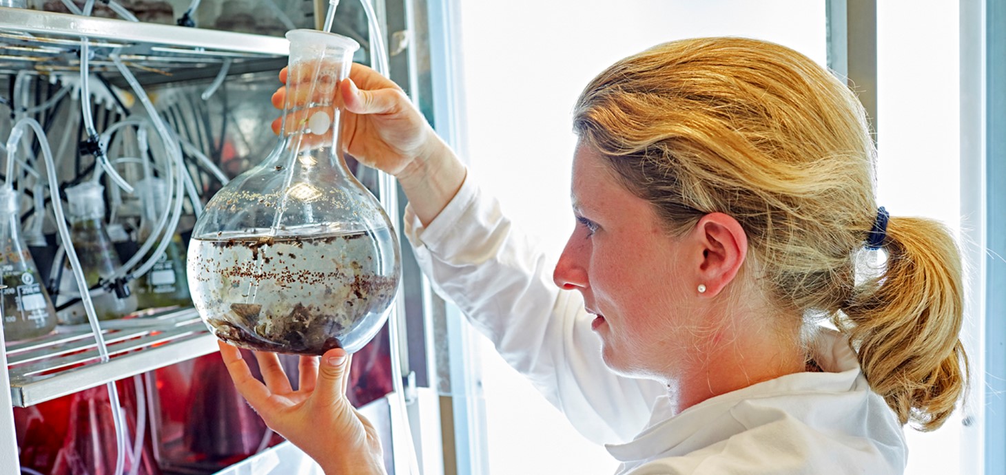 . A woman in a lab coat is holding a beaker