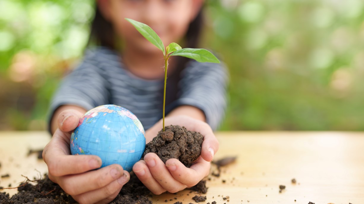 A photo of a girl holding a plant and globe model in the palm of her hands. Credit: SUKJAI PHOTO