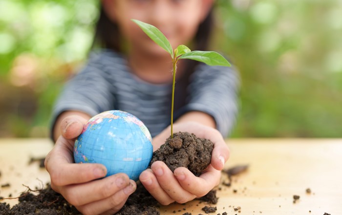 A photo of a girl holding a plant and globe model in the palm of her hands. Credit: SUKJAI PHOTO