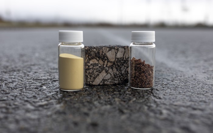 Vials of bio-based spore microcapsules (left) and waste-based capsules (right) for self-healing asphalt on a road. In the centre, is a sample of asphalt mixture. Credit Swansea University