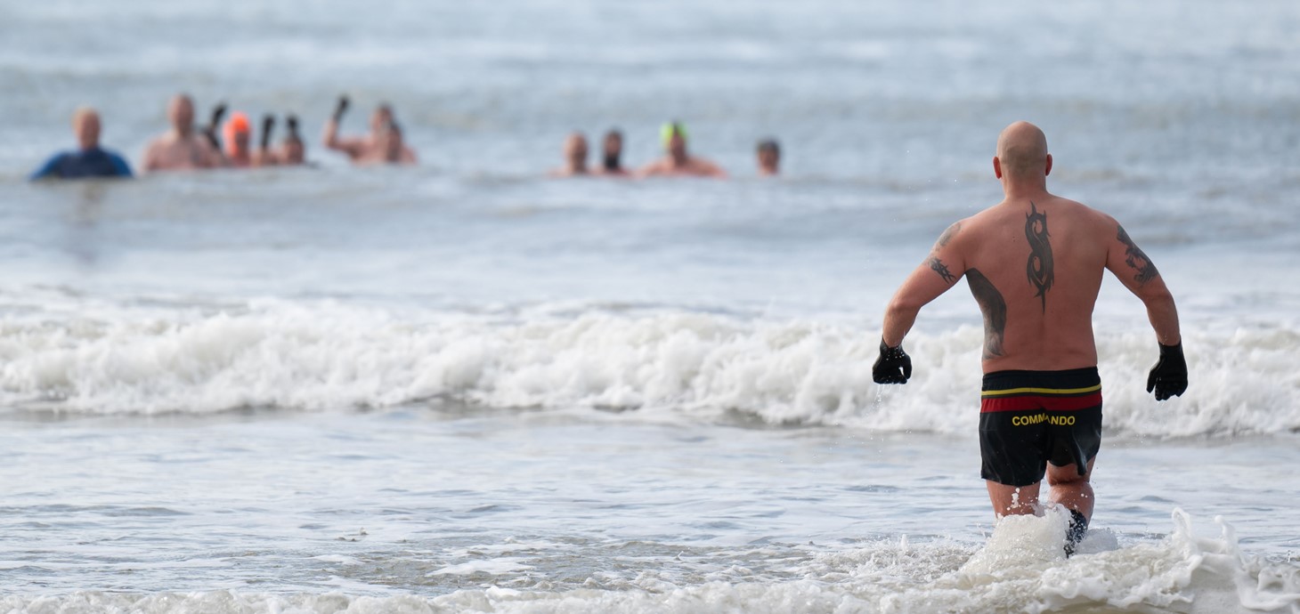 A man walking into the sea towards a group of people already in the sea