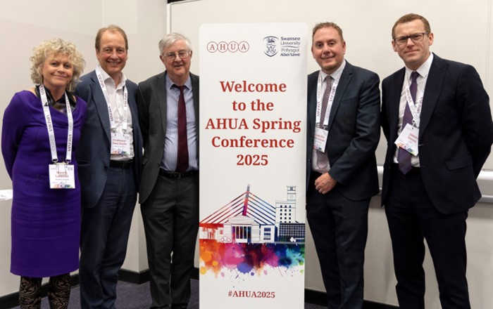 Five smartly dressed people - four men and one woman - standing alongside a conference pop-up banner.