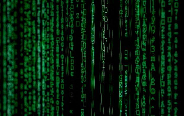 Green digital code characters cascade down a black screen, resembling the matrix-style computer code from the Matrix movie franchise.