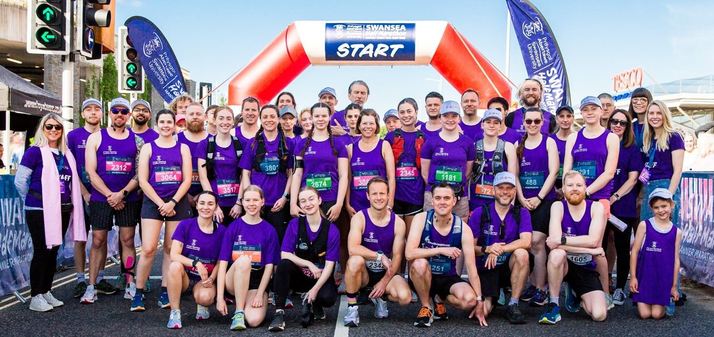 Large group of runners lined up underneath the starting line of a race