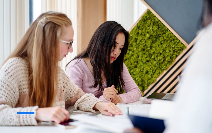 Two young women sitting side by side at a desk looking at a laptop screen