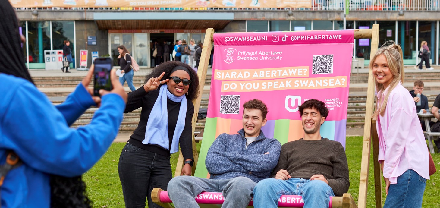 A small group of happy-looking students sitting on a giant, colourful deckchair outside Fulton House