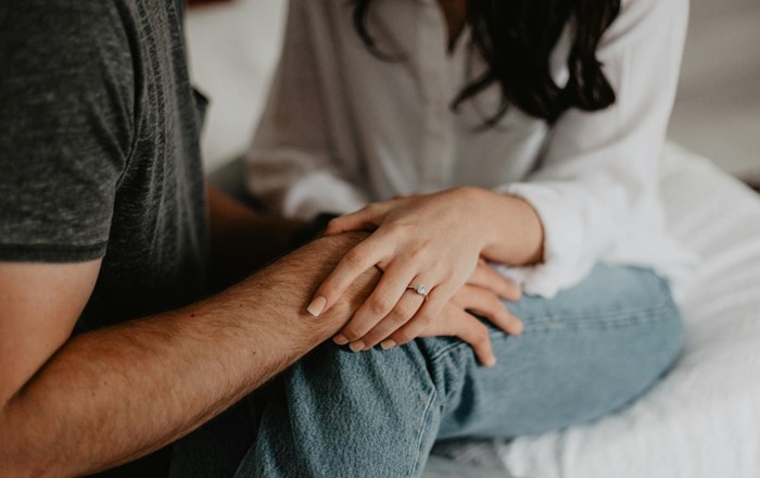 A man and woman holding hands; the woman is wearing an engagement ring. 