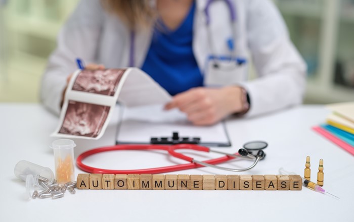 A wooden sign with the words 'autoimmune disease' is on a desk in front of a doctor who is reviewing information on autoimmune diseases.
