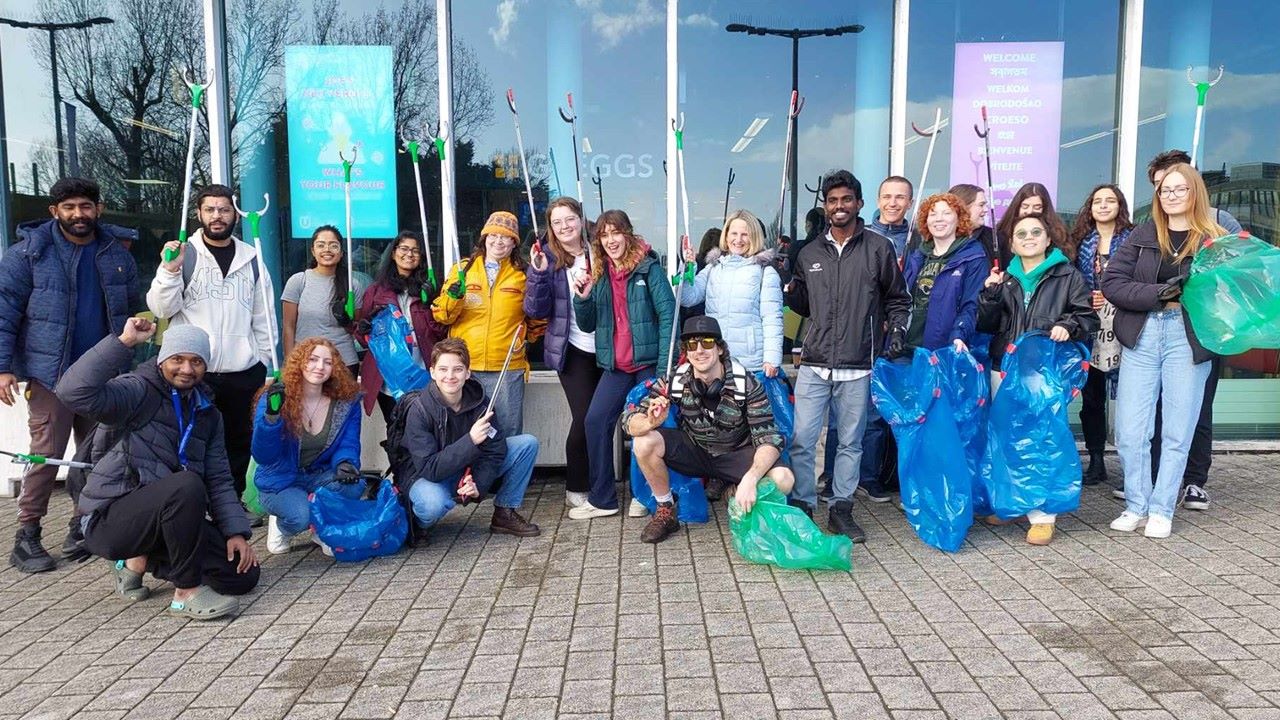 Group of students outside a building holding rubbish bags and litter pickers.