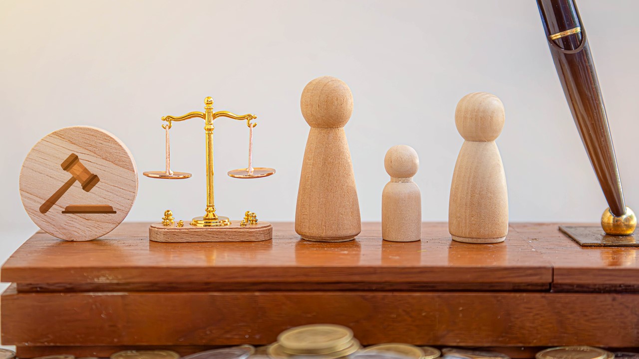 Scales of justice, gavel, three wooden figures and a pen on a wooden stand.
