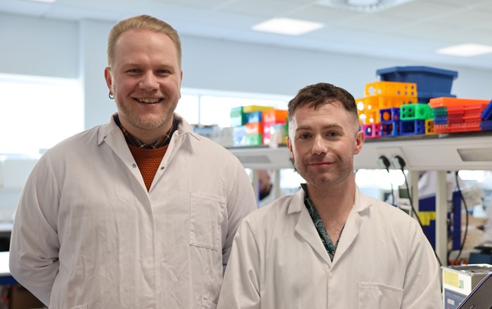 Two men wearing white coats standing in a laboratory.