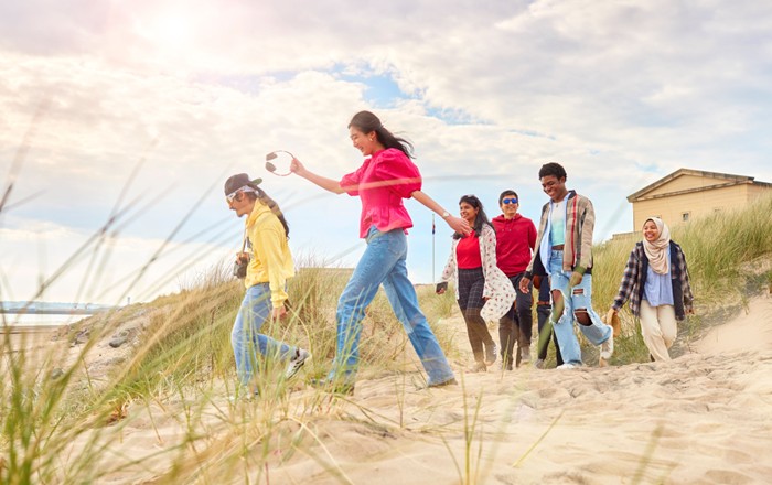 A group of smiling students walking on the back on a sunny day.