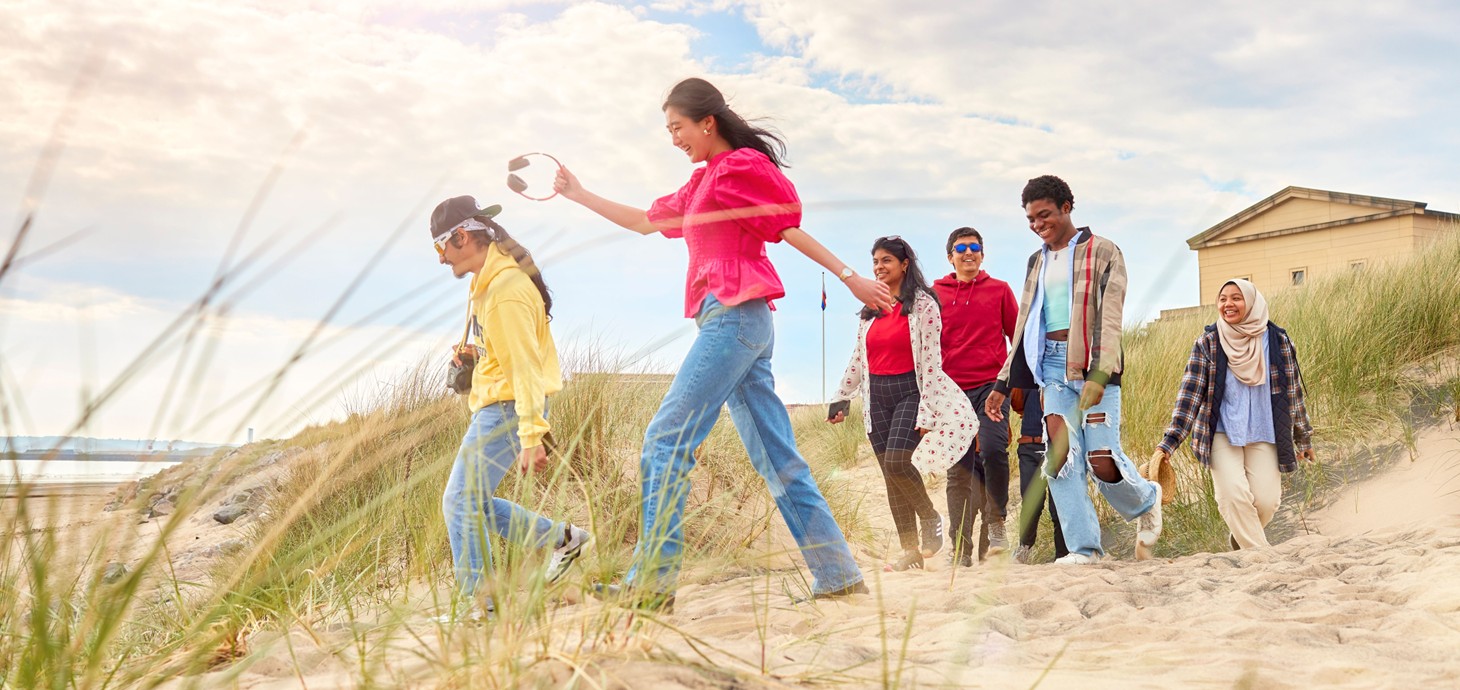 A group of smiling students walking on the back on a sunny day.