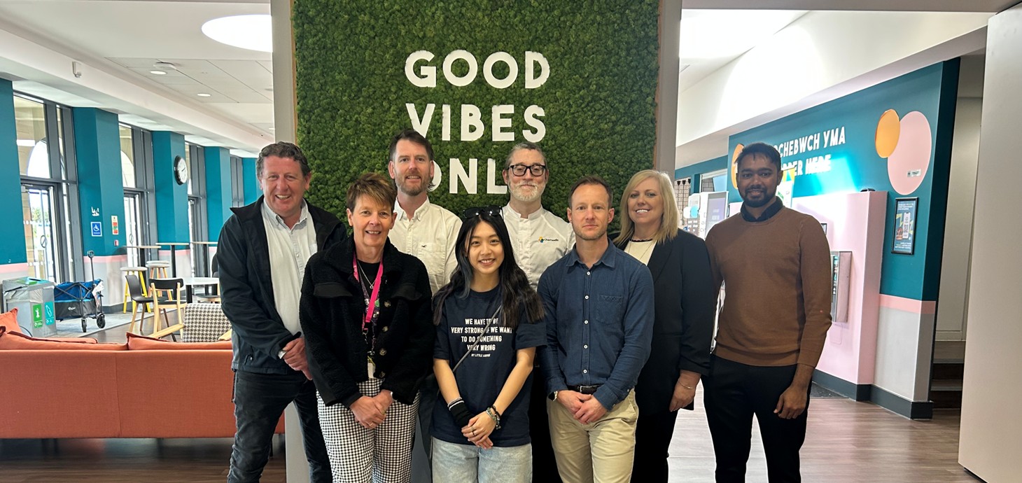 Eight people standing indoors in front of a large sign