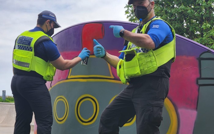 Two police community support officers wearing facemasks holding spraypaint cans