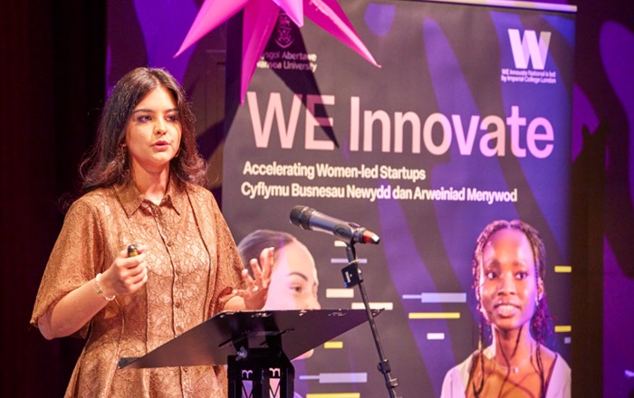 One woman standing at a lectern in front of a large banner.