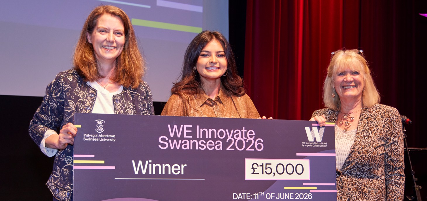 Three woman standing on a stage holding a large cheque between them.