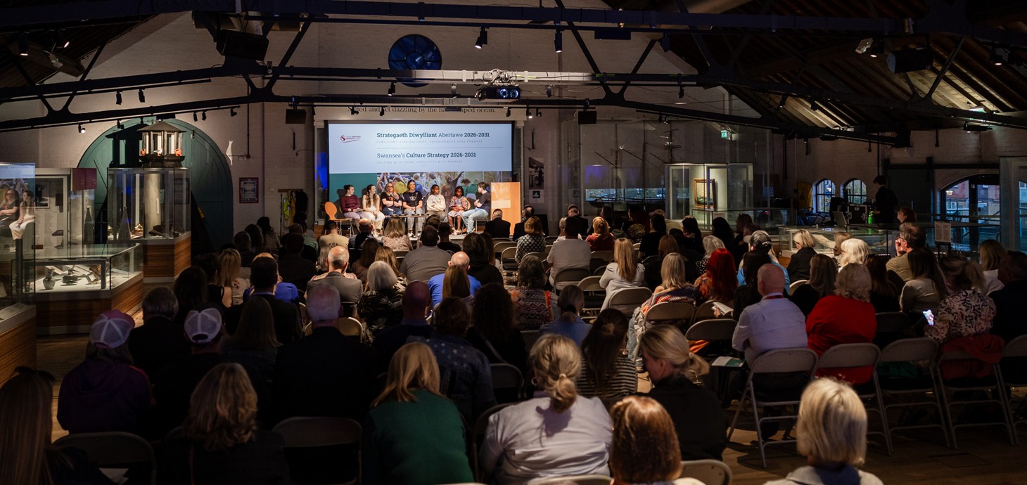 Room of people sitting in a dark room looking towards a stage.