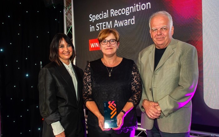 Woman holding an award with man and woman standing either side of her.
