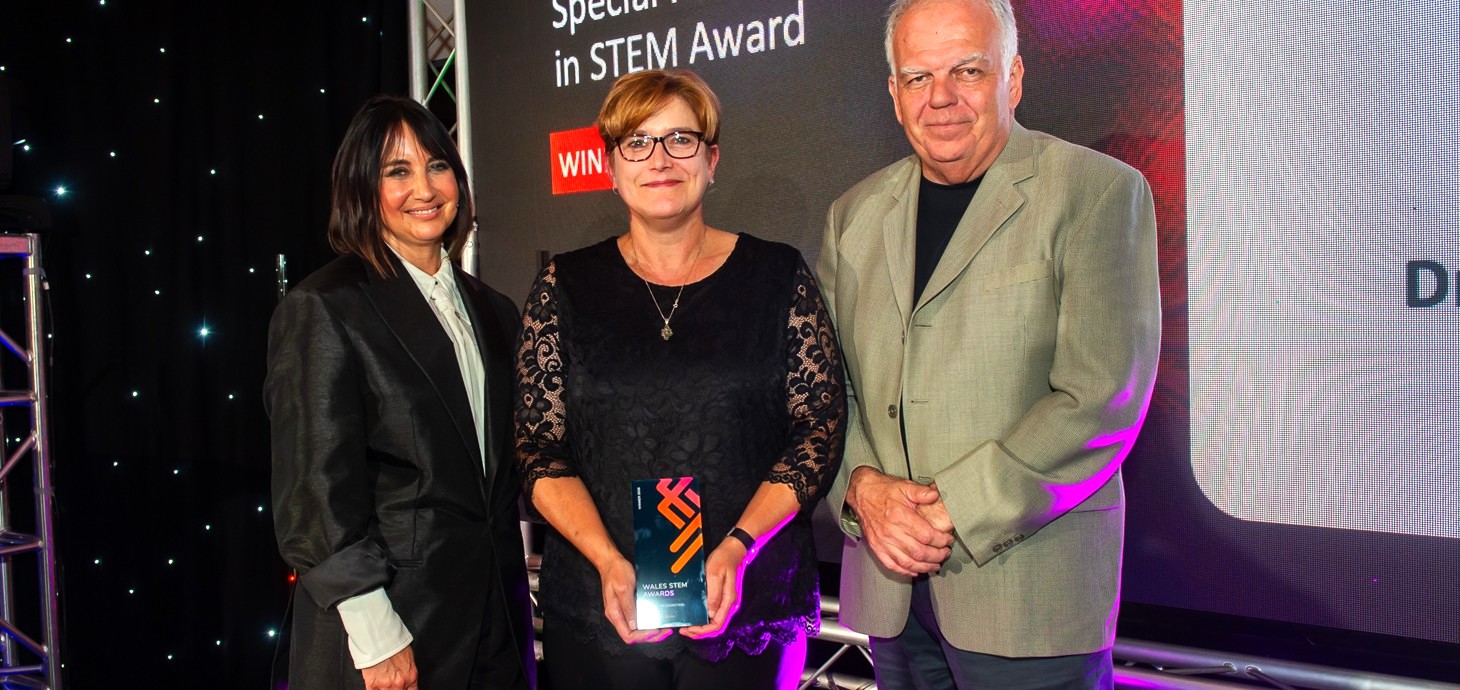 Woman holding an award with man and woman standing either side of her.