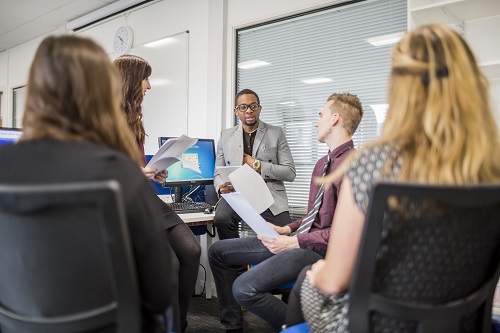 Colleague giving information to others sitting at computer desk