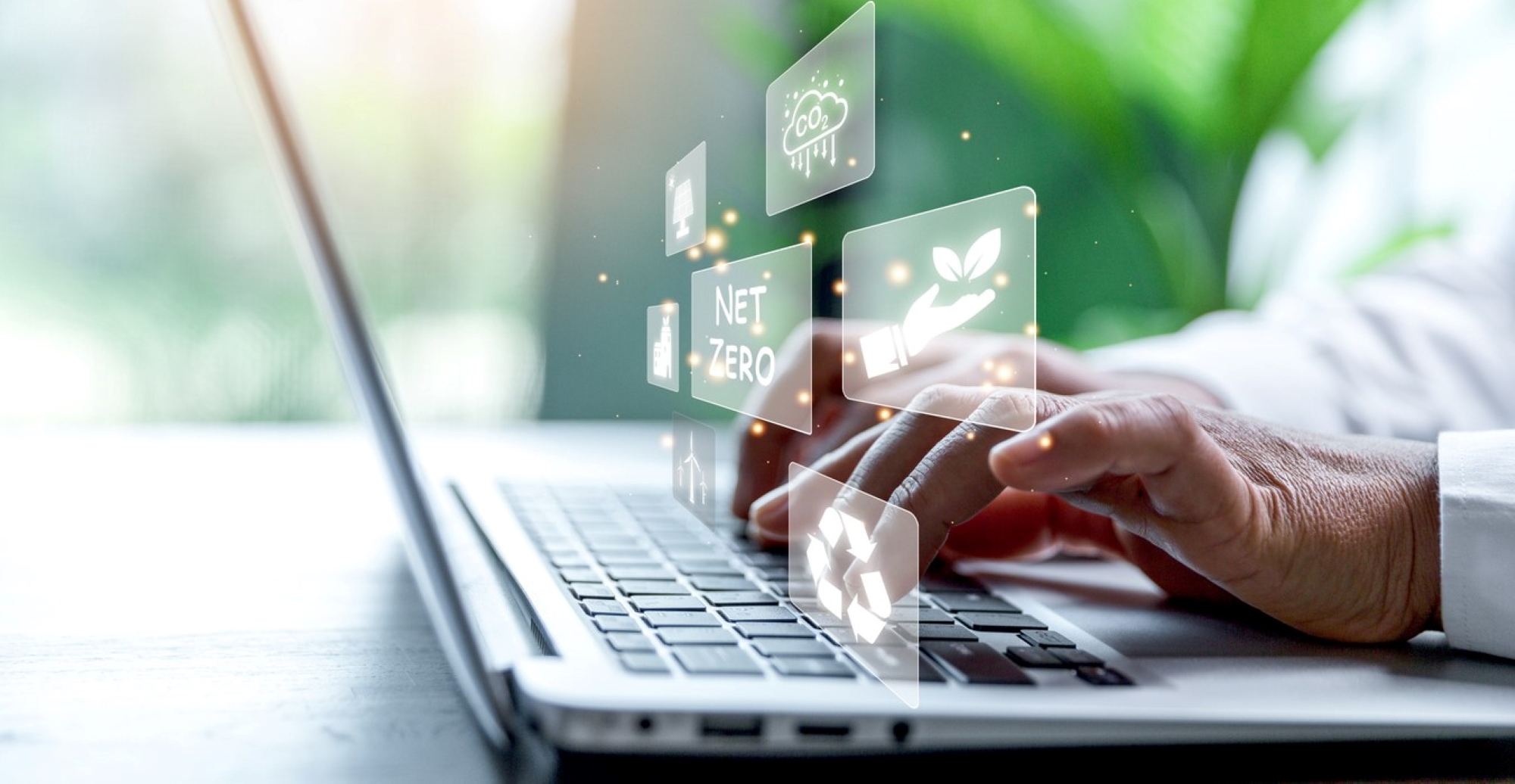 Man's hands typing on a laptop while sustainability icons float above