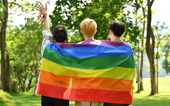 Three people wrapped in a rainbow flag