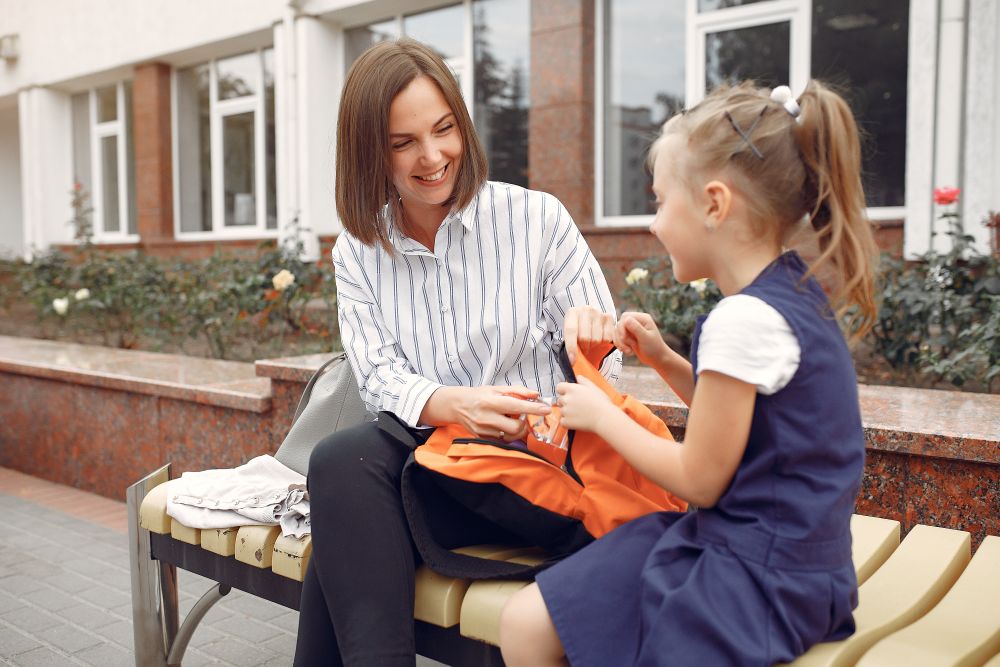Adult helping child with school bag outside a school building
