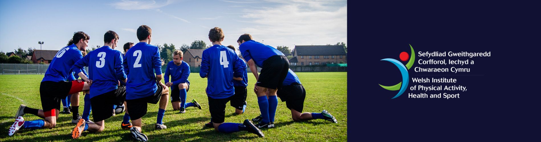 A football team crouch on the ground ready to receive a brief from the captain. 