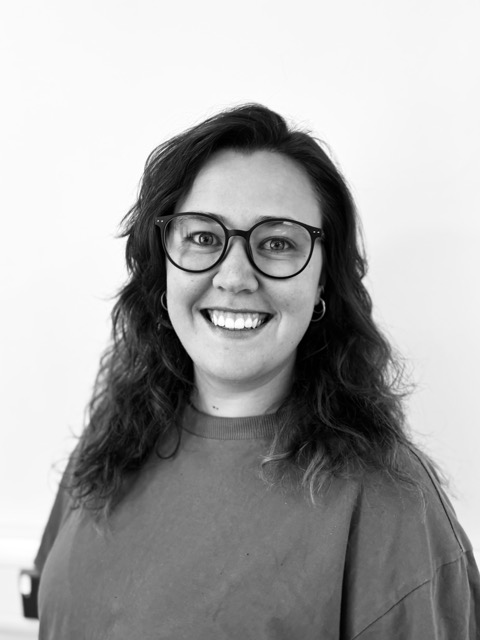 Black and white photo of Hannah wearing round glasses with long, dark wavey hair