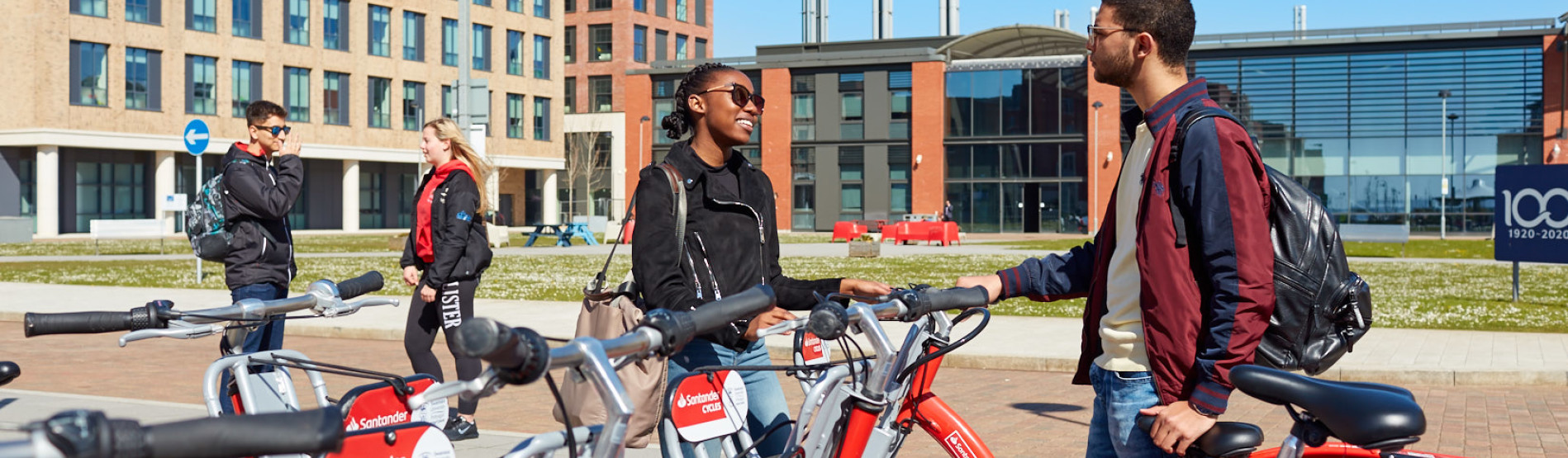 Four students on Bay Campus chatting near the bike hire stand.