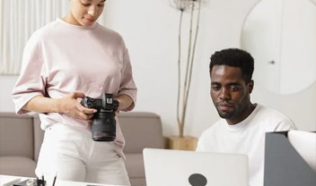 A student holding a camera stood next to another student using a laptop