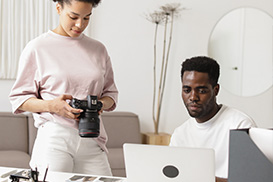 A student holding a camera stood next to a student using a laptop