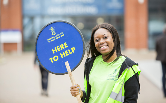 Student holding 'Here to help' sign