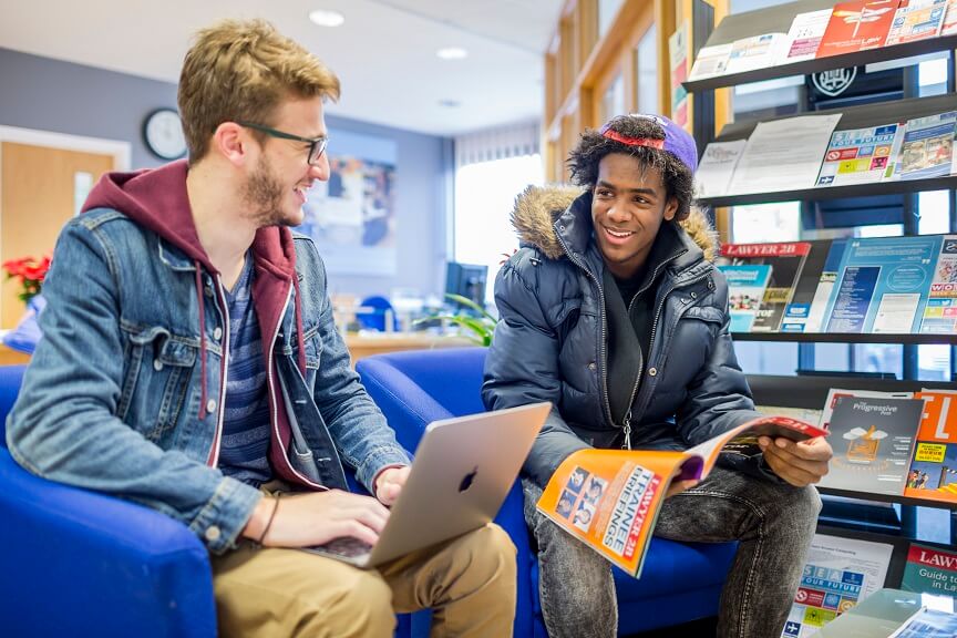 Two males sat with a magazine and laptop