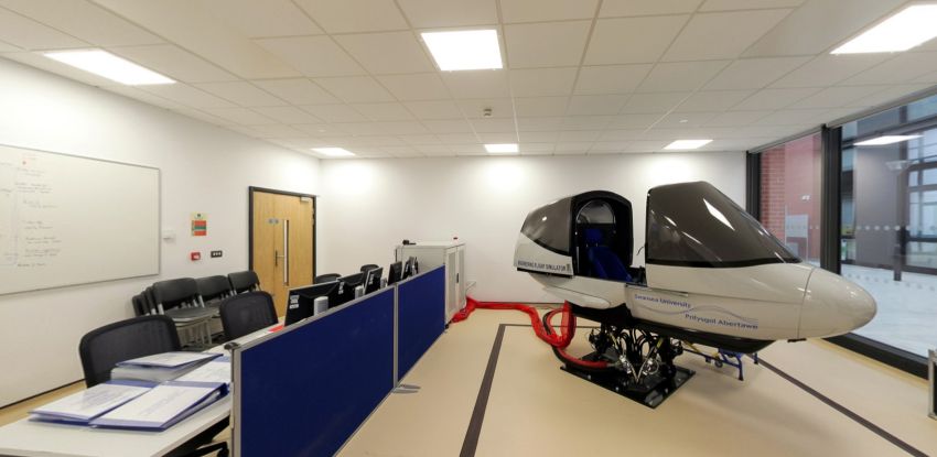 Flight simulator lab with cockpit simulator, desks, and computers