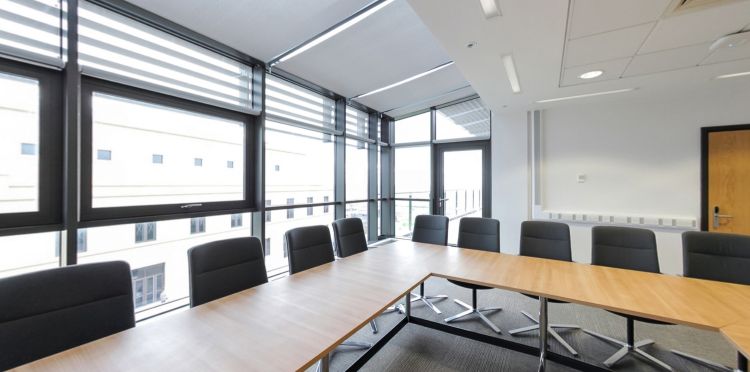 Bright meeting room with tables, chairs, and large windows overlooking campus