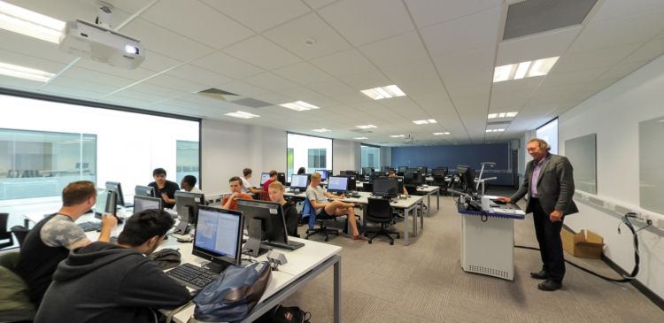 Computer lab with desks, large projection screen, and a person at the lectern