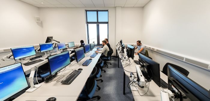 Students working at computers in a university PC lab with modern workstations