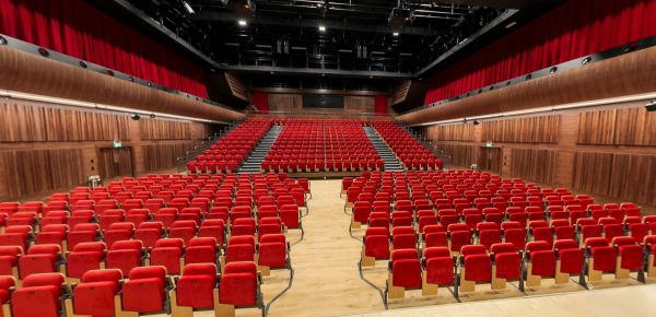Modern auditorium with red seating, timber walls and central aisle