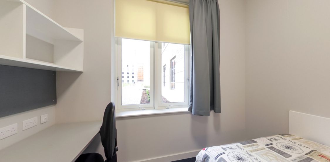Modern student bedroom with desk, shelving, bed and window with blinds
