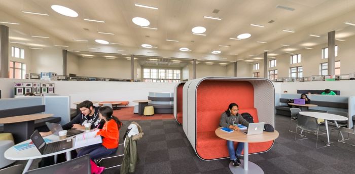 Library study area with booths, tables and students using laptops